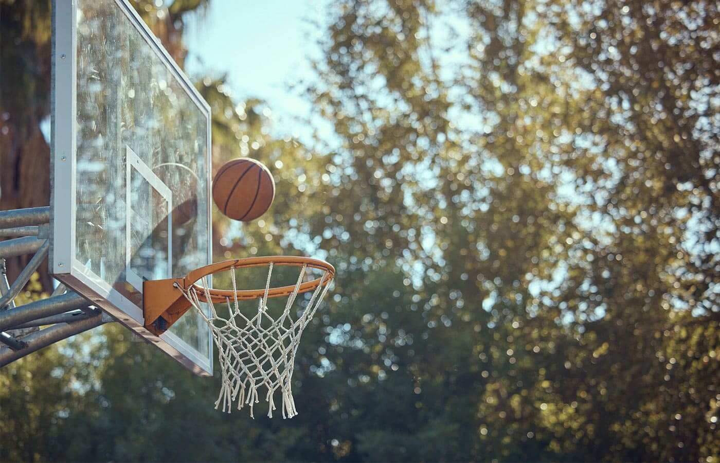 A basketball being thrown at a hoop during a sunny day