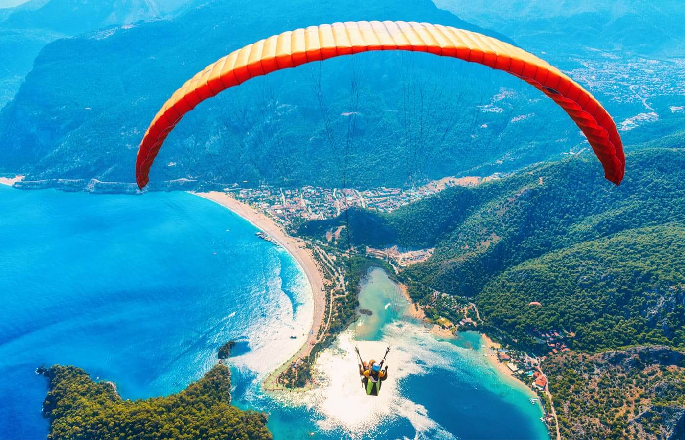 A paraglider flying above a coastal city on a clear sunny day