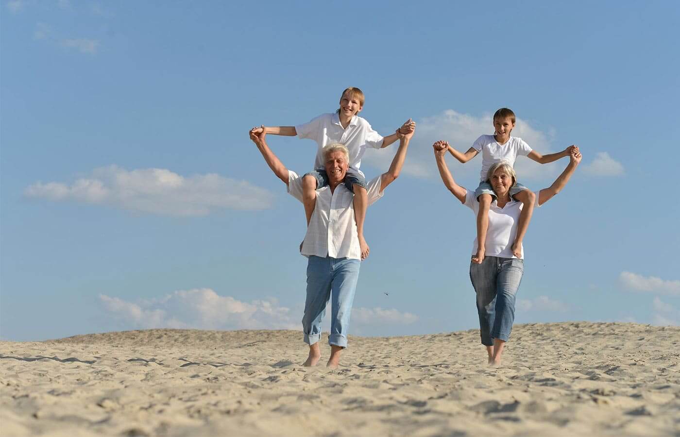 Grandparents carrying grandchildren on their shoulders on a sandy beach